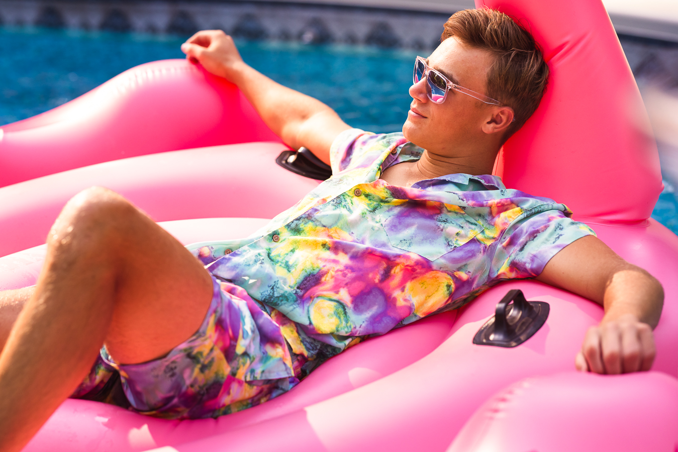 this vibrant, colorful, fun image of this senior as he floats on his pink flamingo floaty in a vibrant, colorful swim suit captured by Creative Senior Portrait Photographer, lisa rhinehart