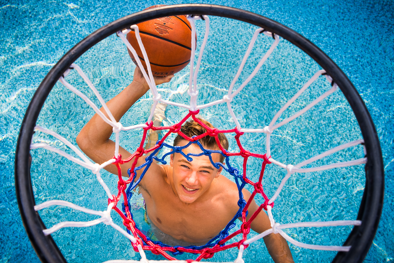 Colorful, vibrant, creative image of this senior as he gets ready to dunk the basketball into the net in his swimming pool captured by Creative Senior Portrait Photographer, lisa rhinehart