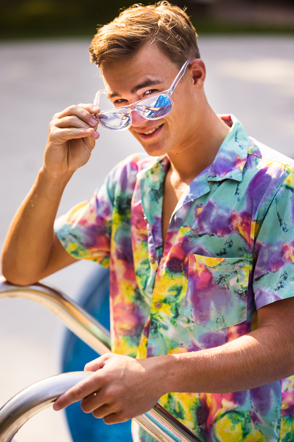 lisa rhinehart, captures this fun, vibrant traditional portrait of this senior as he gets out of his pool and peeks over his sunglasses during this senior session 