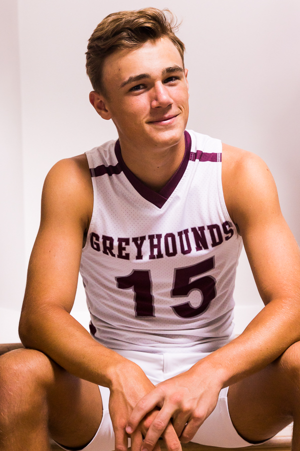 senior portrait photographer, lisa rhinehart, captures this traditional portrait of this senior in his basketball jersey and shorts as he smiles at the camera 
