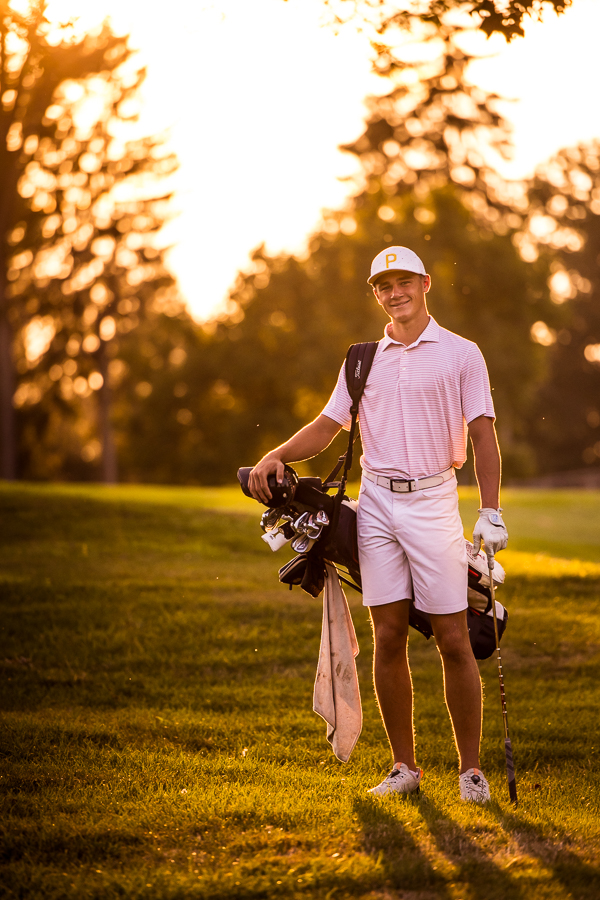 chambersburg senior portrait photographer, lisa rhinehart, captures this traditional, vibrant image of this senior as he stands on the golf course with his clubs and bag in his pink golf attire at the Chambersburg country club 