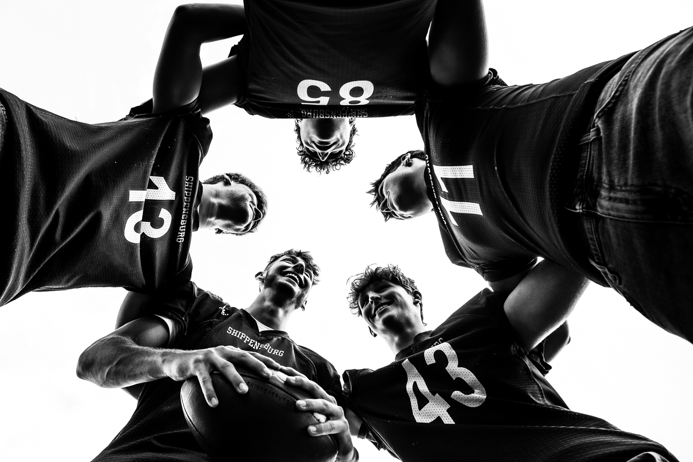 black and white image of high school football players as they stand in a huddle together during this outdoor football photo session 