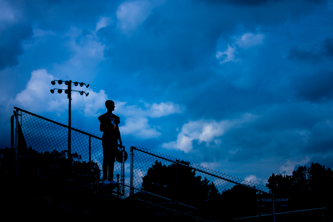 creative, vibrant image of this Shippensburg high school senior as he stands on the bleachers facing his football field while a storm rolls in behind him during his outdoor football photo session 