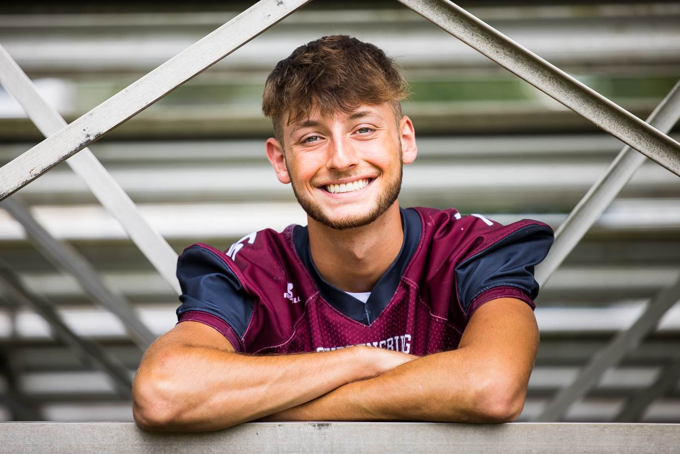 local shippensburg photographer, lisa rhinehart, captures this traditional image of this football player leaning on the bleachers smiling at the camera 