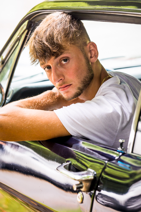 image of this high schooler as he looks out the window of his 1966 mustang back at the camera with his arm leaning out 
