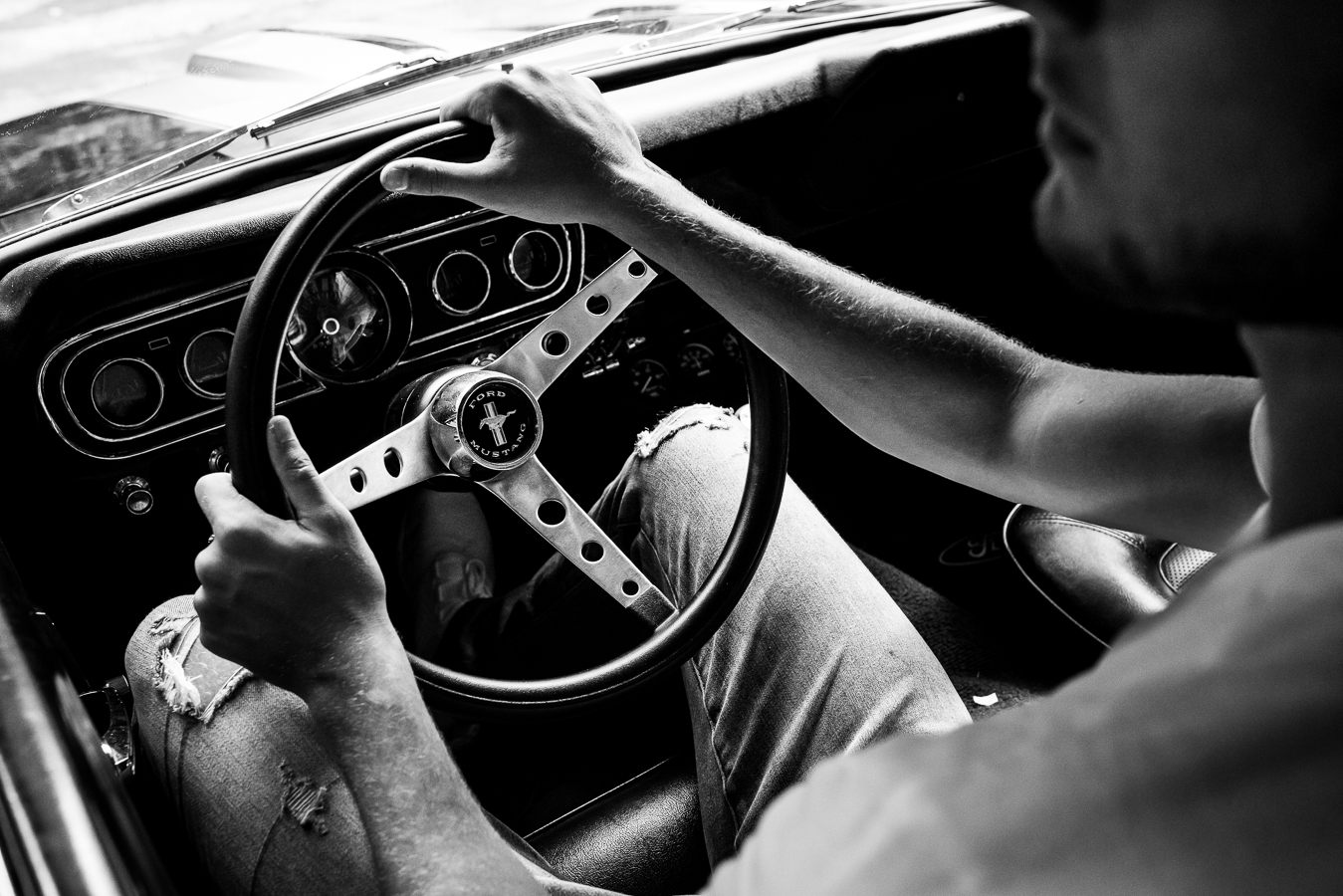 unique, creative black and white image of this senior as he sits in his car with his hands on the wheel 