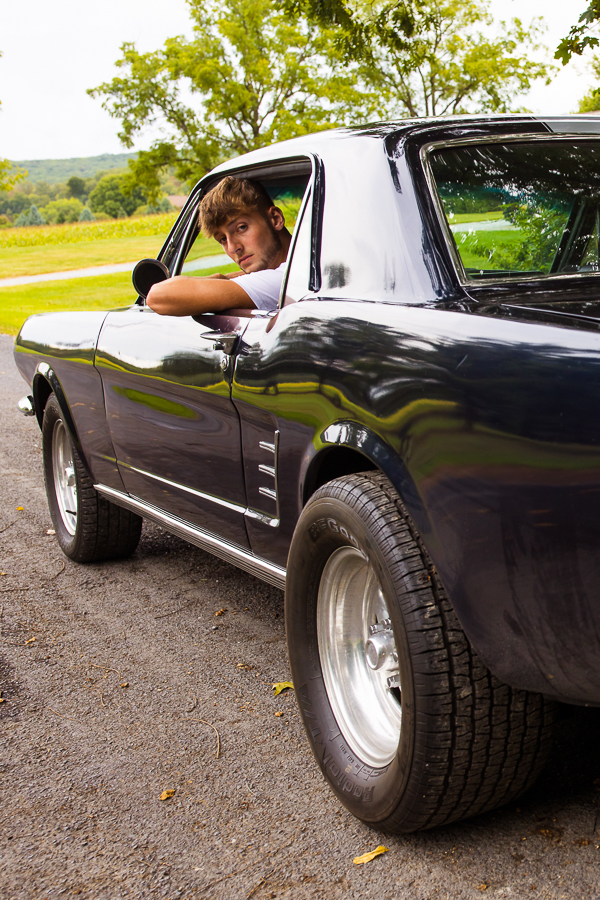 creative, unique image of this hs senior as he drives off from his session in his 1966 mustang as he looks back towards the camera