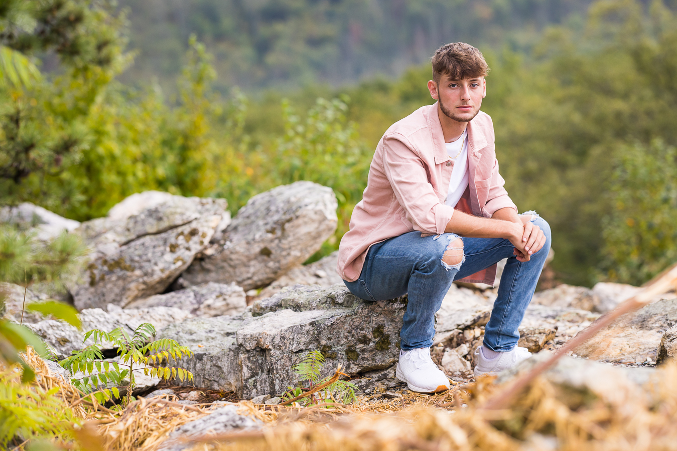 traditional portrait of this senior as he sits on the rock overlook with his arms on his knees during this outdoor session 