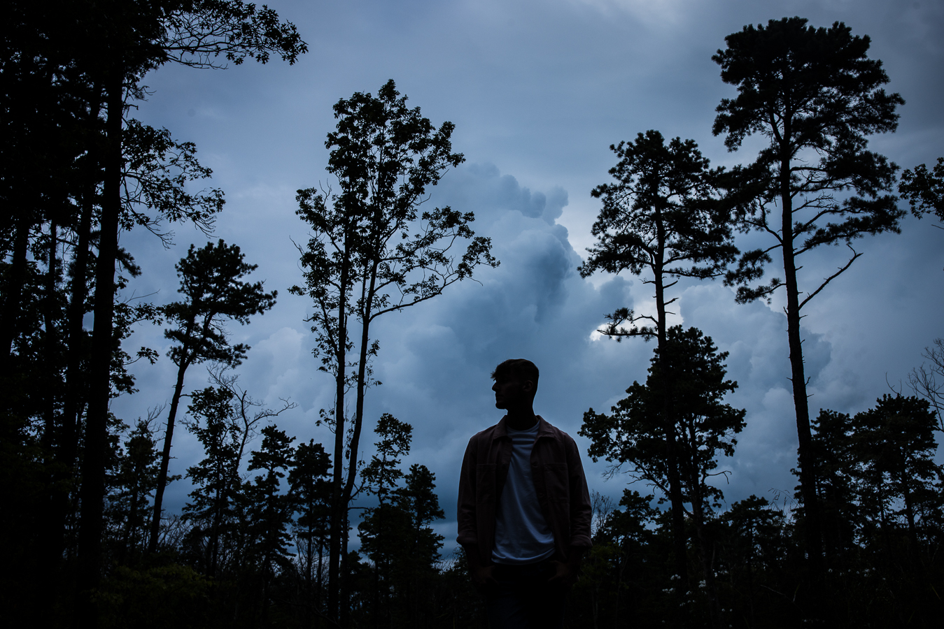 creative High school Senior Portrait Photographer, lisa rhinehart, captures this image of this senior as he stands amongst the trees as a storm rolls in behind him during this outdoor senior portrait session