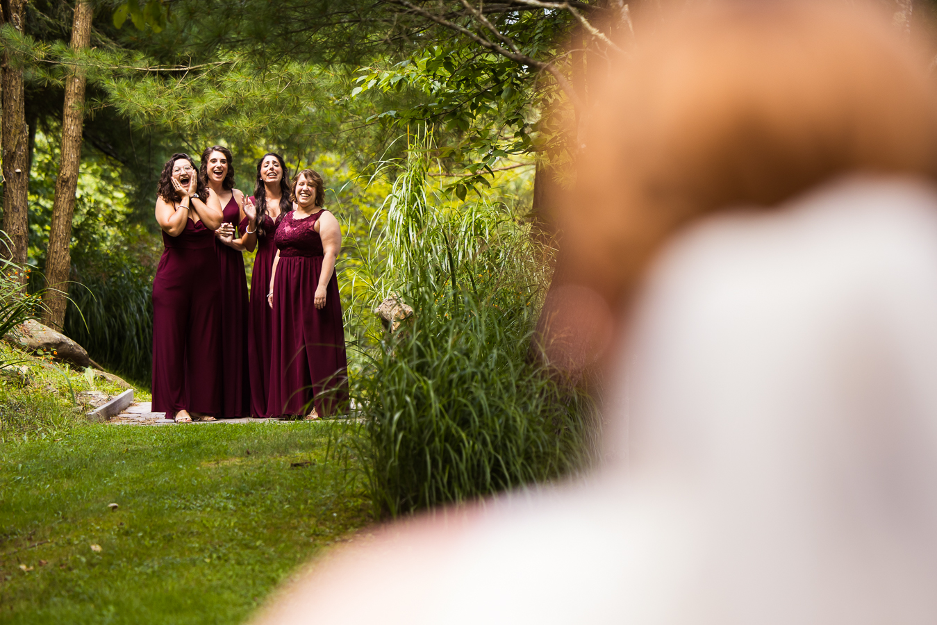Oak Lodge Wedding Photographer, rhinehart photography, captures this outdoor first look with the bridesmaids who are smiling from ear to ear as they see the bride for the first time surrounded by greenery at this outdoor wedding 