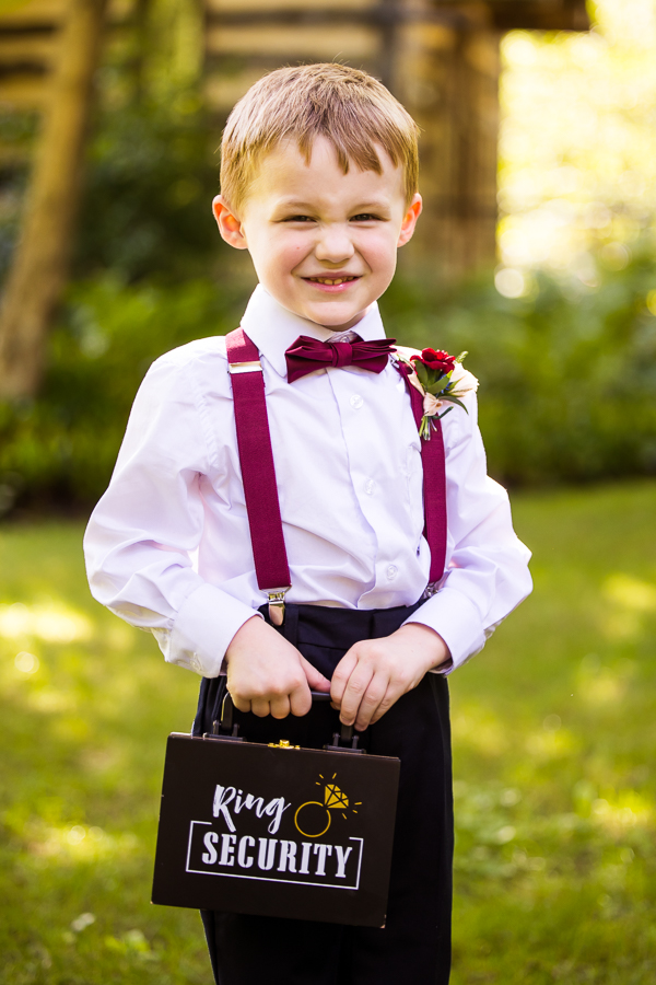 lisa rhinehart, captures this fun, friendly image of the ring bearer as he smiles at the camera while holding his ring security box before the wedding ceremony in stahlstown pa 