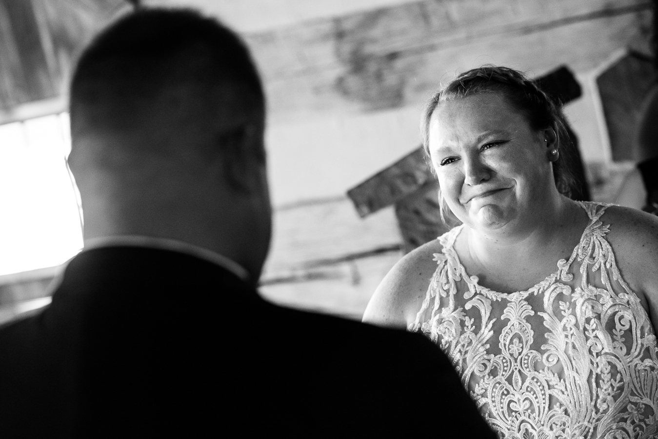 black and white emotional image of the bride as she looks at the groom with tears in her eyes and a smile on her face as they have their wedding ceremony inside of the chapel at oak lodge in stahlstown, pa 