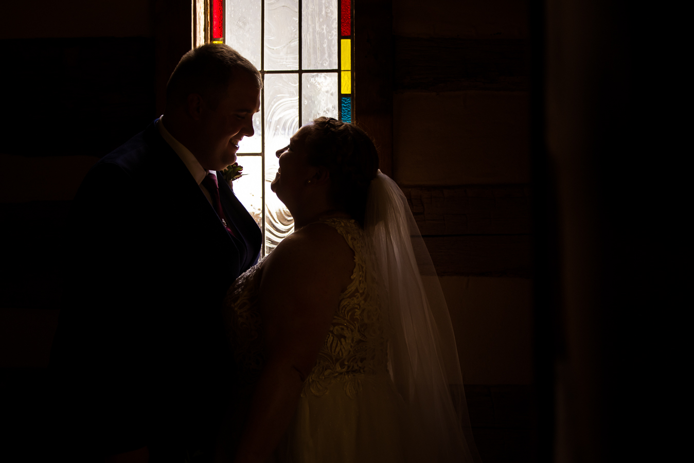 unique, creative silhouette image of the bride and groom as they stand beside a colorful stained glass window 