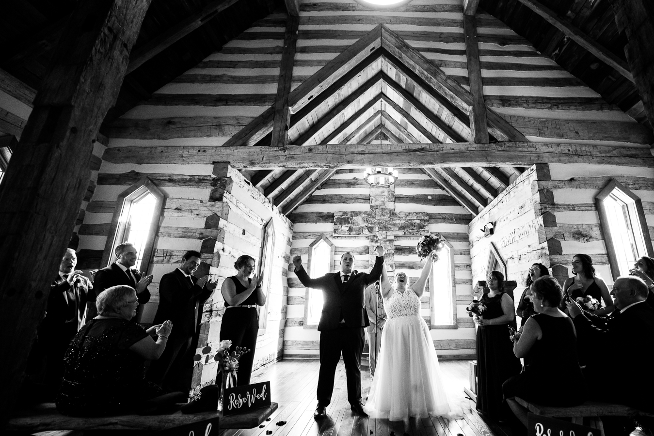 Oak Lodge Wedding Photographer, rhinehart photography, captures this happy moment when the bride and groom are finally married and cheering as their family and friends clap for them inside of this cozy log chapel on the property of oak lodge 