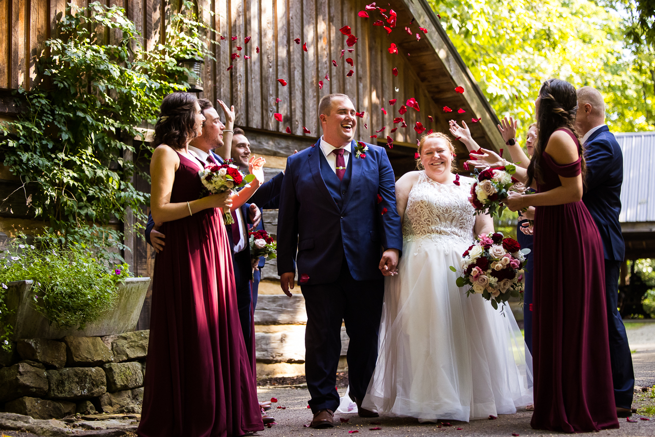 fun, colorful, vibrant image of the bride and groom as they walk between their bridal party as they throw vibrant red petals while the bride and groom smile and laugh after their wedding ceremony in stahlstown pa 