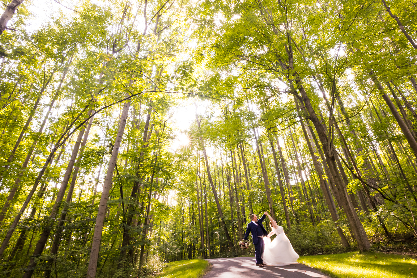 Oak Lodge Wedding Photographer, rhinehart photography, captures this romantic portrait of the couple as they walk through the woods while spinning the bride around as they are surrounded by the vibrant, tall green trees and landscaping 