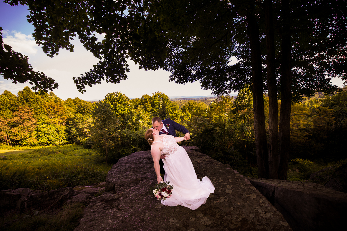 Oak Lodge Wedding Photographer, rhinehart photography, captures this stunning, unique image of the bride and groom as they stand on the ledge kissing surrounded by the trees and mountain views during their romantic portrait session