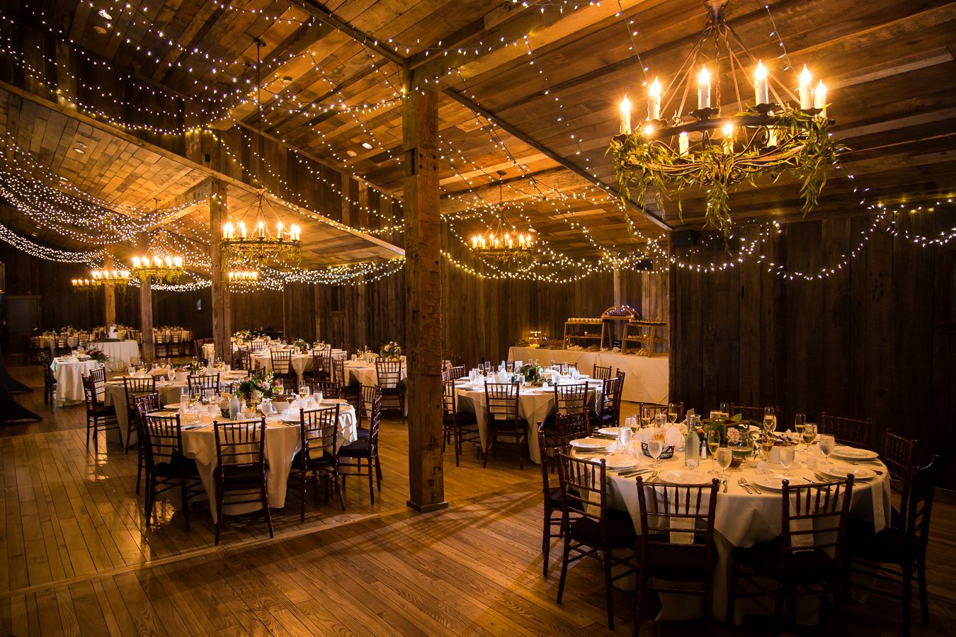 image of the inside of the barn all decorated with twinkle lights and decor for this oak lodge wedding reception which also includes the Pittsburgh cookie table tradition