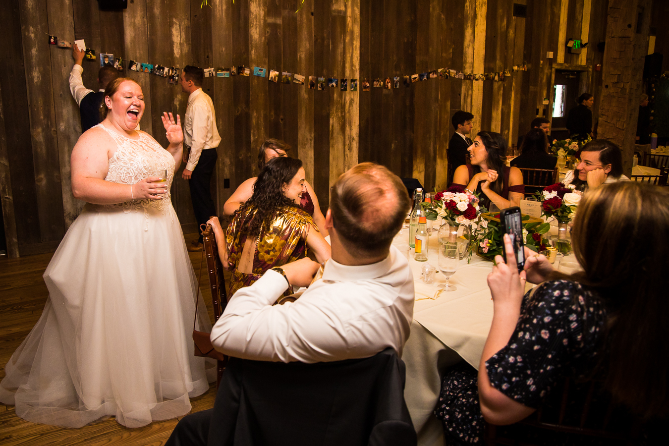 fun, candid image of the bride interacting with guests during this indoor wedding reception in stahlstown pa, with a clothesline picture timeline in the background behind her 