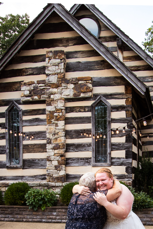 image of the bride and her mom sharing their mother daughter dance outside of the chapel made out of stunning log work and a giant rock cross behind them 