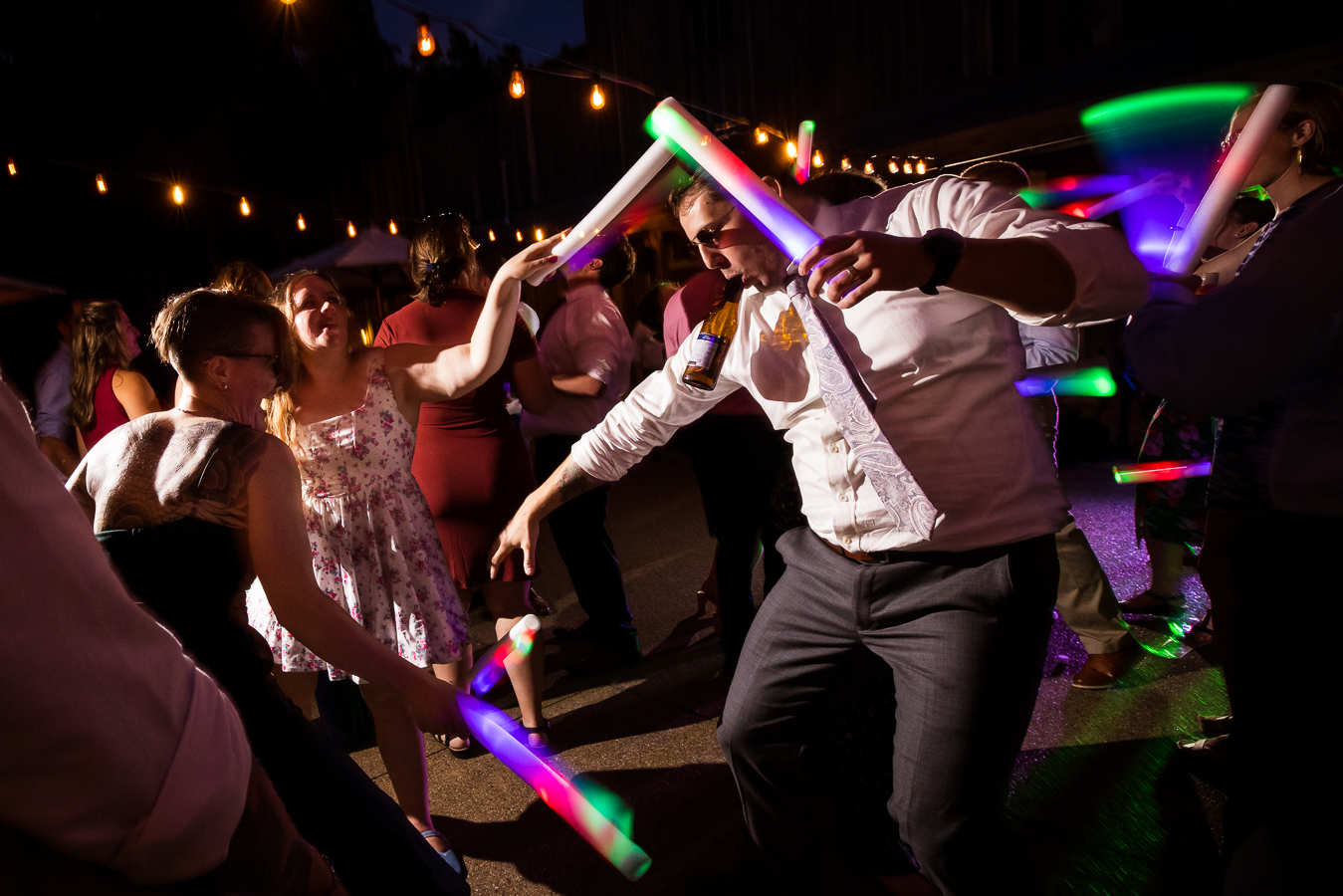 fun, creative Oak Lodge Wedding Photographer, rhinehart photography, captures this fun, candid, vibrant image of friends at the wedding as they dance with each other during this outdoor wedding reception with giant glow sticks that light up the dance floor 