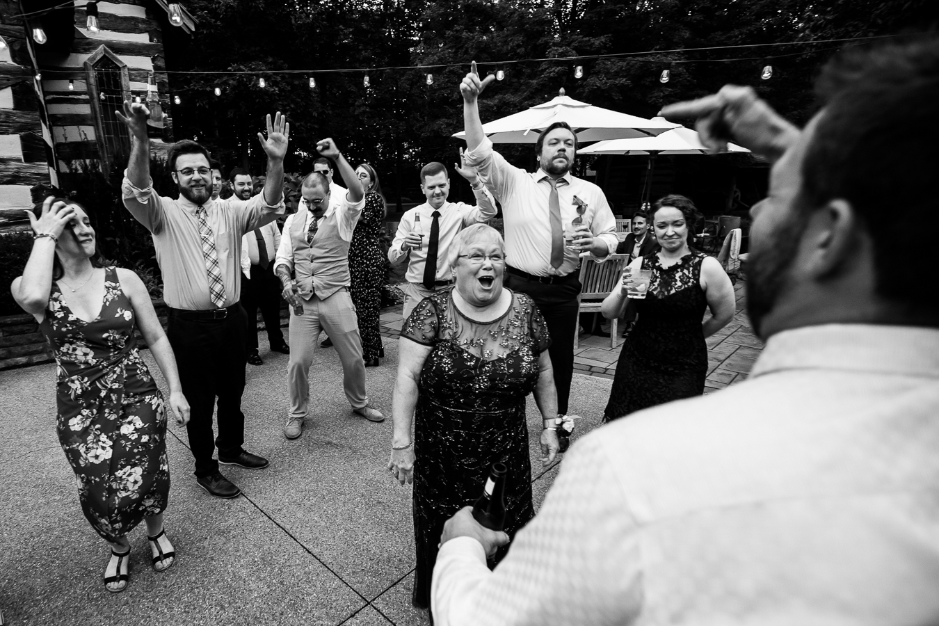 black and white image of guests dancing and cheer each other on as they get this unique outdoor wedding reception started