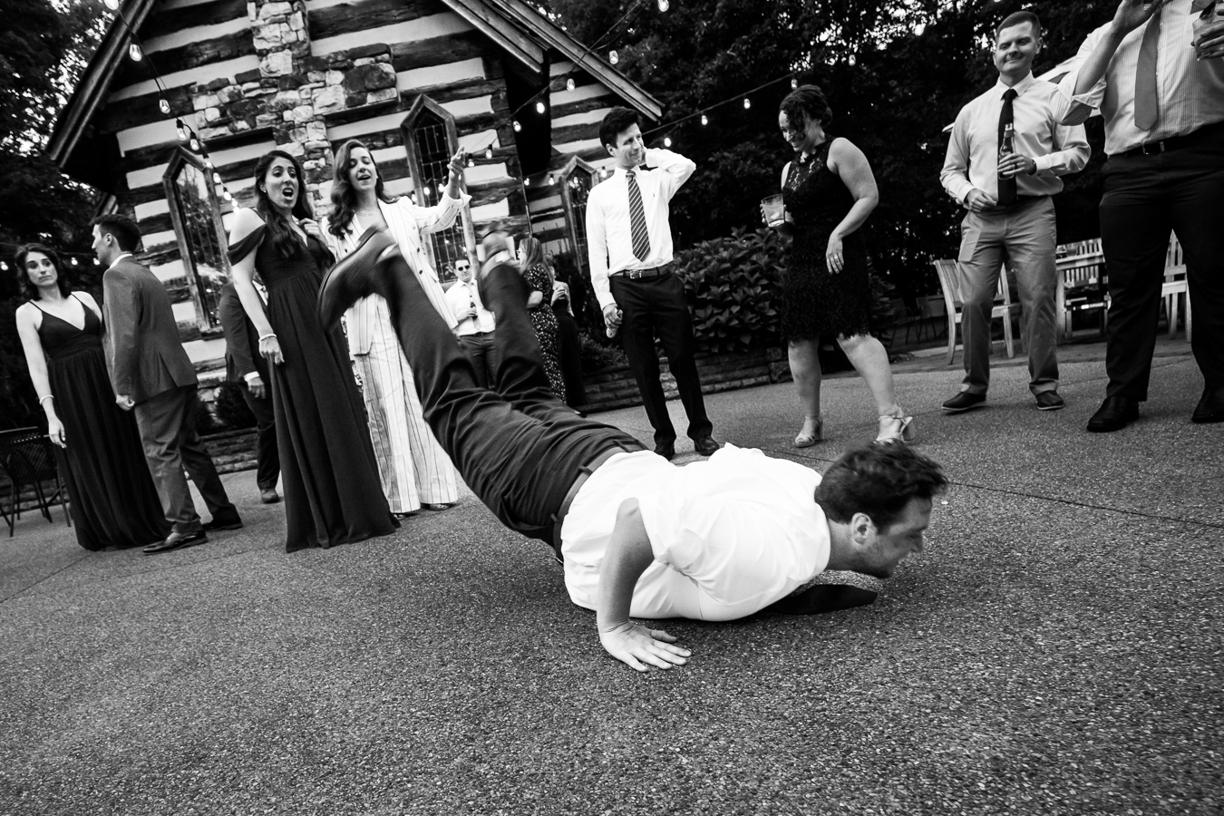 fun Oak Lodge reception photographer, rhinehart photography, captures this black and white image of a guest doing the worm as guest smiles and cheer him on from afar during this outdoor wedding reception 
