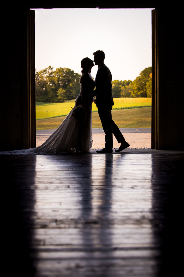 creative wedding photographer, Lisa Rhinehart, captures this silhouetted image of the couple as they almost kiss while standing between the barn doors in the ceremony space at alpine acres located in warfordsburg, pa 