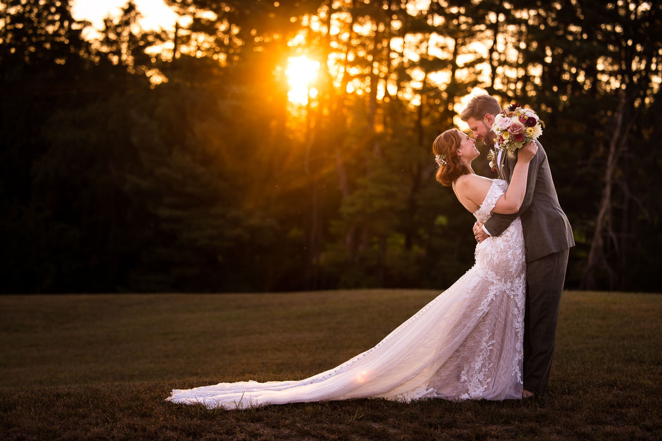 creative maryland wedding photographer, lisa rhinehart, captures this image of the bride and groom as they stand in the grass field embracing one another while the sun beams through the trees behind them during golden hour at this branding photography session 