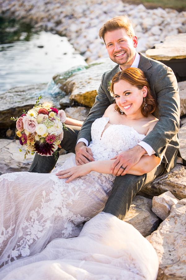 image of the bride and groom as they sit on the rocks near the vibrant blue pond at the new wedding venue in warfordsburg pa, alpine acres