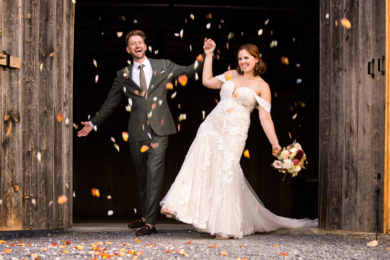 fun, colorful, vibrant image of the bride and groom as they exit the barn doors as colorful petals fall around them provided by iron willow floral designs for this branding photography session 