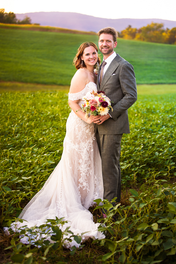 traditional portrait of the bride and groom as they stand beside one another in a field of crops at this rustic wedding venue 