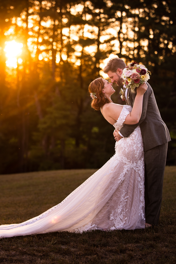 creative wedding photographer, lisa rhinehart, captures this image of the bride and groom as they embrace each other in the open grass field at alpine acres while the sun sets behind them through the trees in warfordsburg pa 