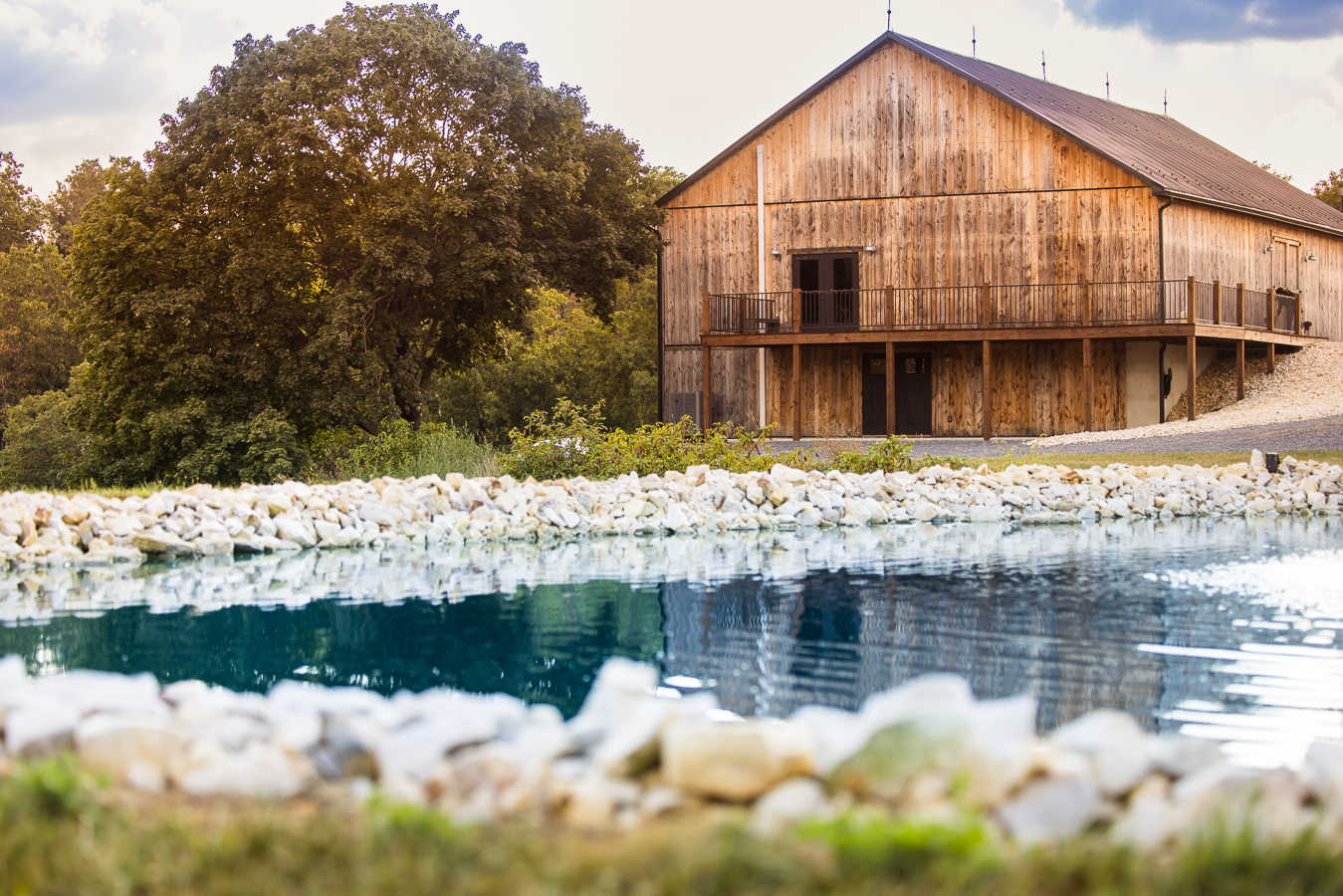 image of the barn and vibrant blue pond located at alpine acres, a new wedding venue in south central pa, that was photographed during this branding photography session 
