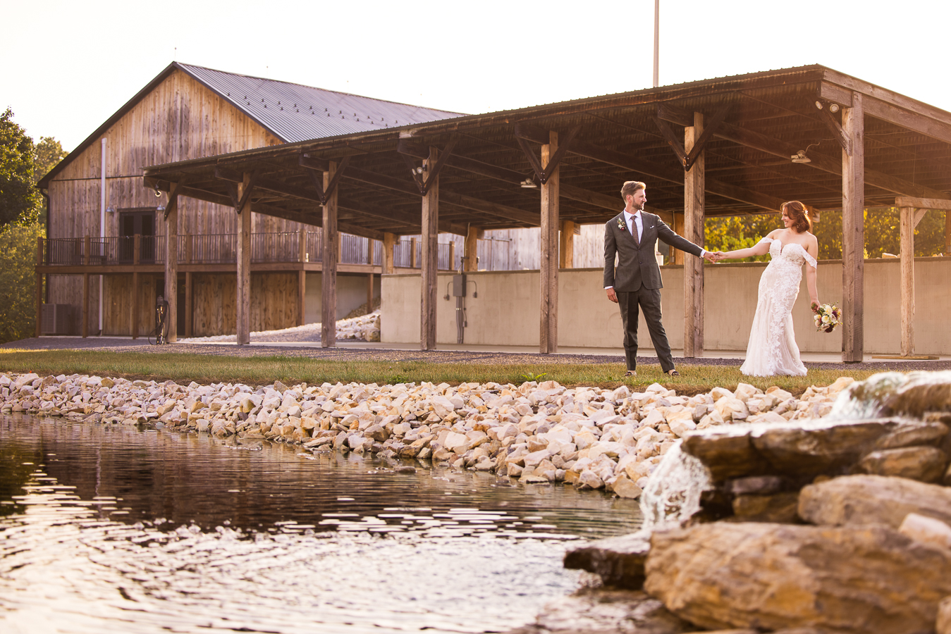 image of the couple as they hold hands and walk around the pond with he barn and pavilion behind them at alpine acres one of Central PA Wedding Venues 