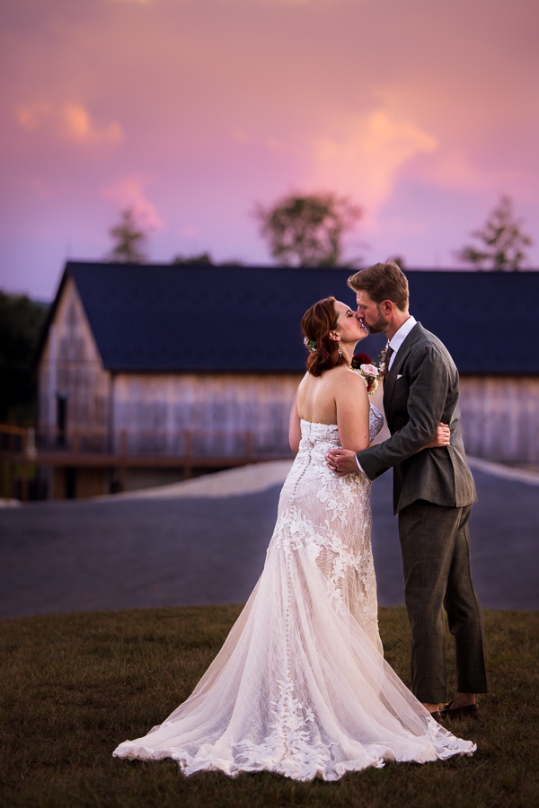 colorful, vibrant, creative image of this couple as they kiss one another during this pink, purple sunset in front of the rustic barn at alpine acres one of the local Central PA Wedding Venues