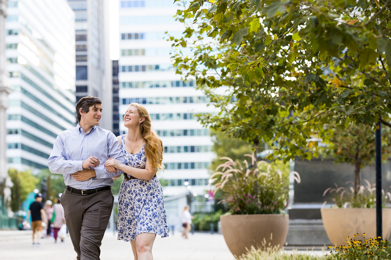philly engagement photographer, rhinehart photography, captures this light, bright traditional image of the couple as they walk down the busy street arm in arm laughing at one another during their engagement session 