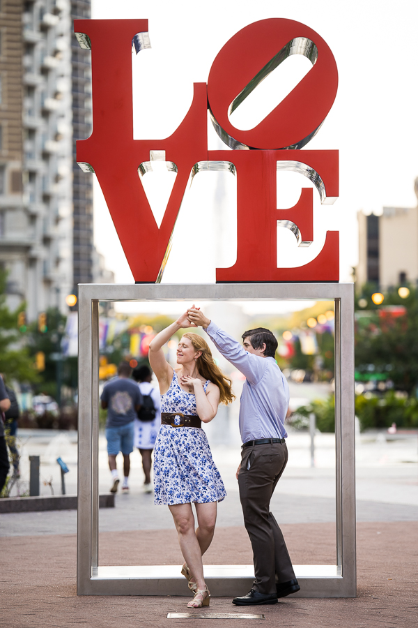 creative, unique image of the couple as they spin around and dance underneath the famous love sign in Philadelphia captured by Creative Philadelphia photojournalism Photographer, rhinehart photography 