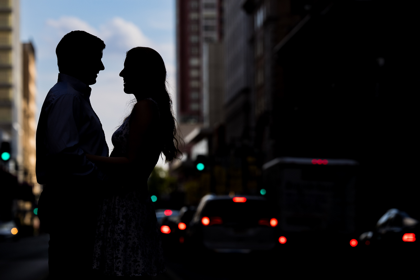 creative, unique silhouetted image of the couple as they smile at each other with he vibrant blue sky behind them and taillights of the cars in the background popping 