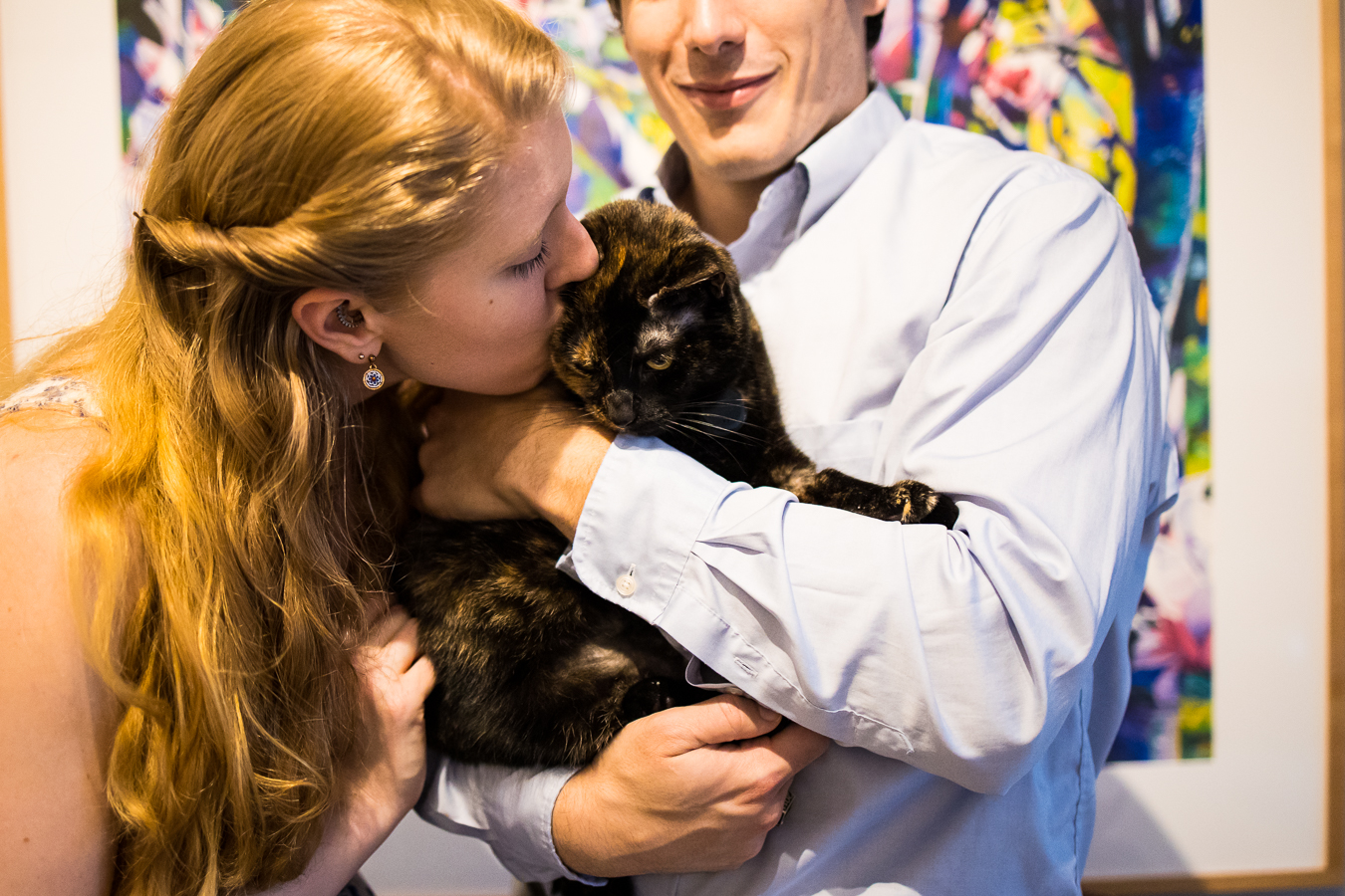 image of the couple as they hold and kiss their cat violet during their engagement session at their apartment 