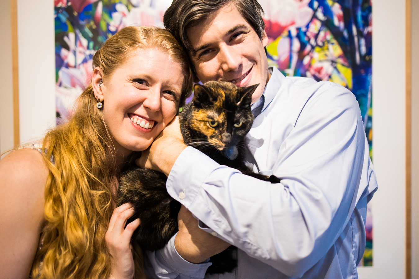 family portrait of the couple with their cat as the cat tries to jump out of their arms during the photo