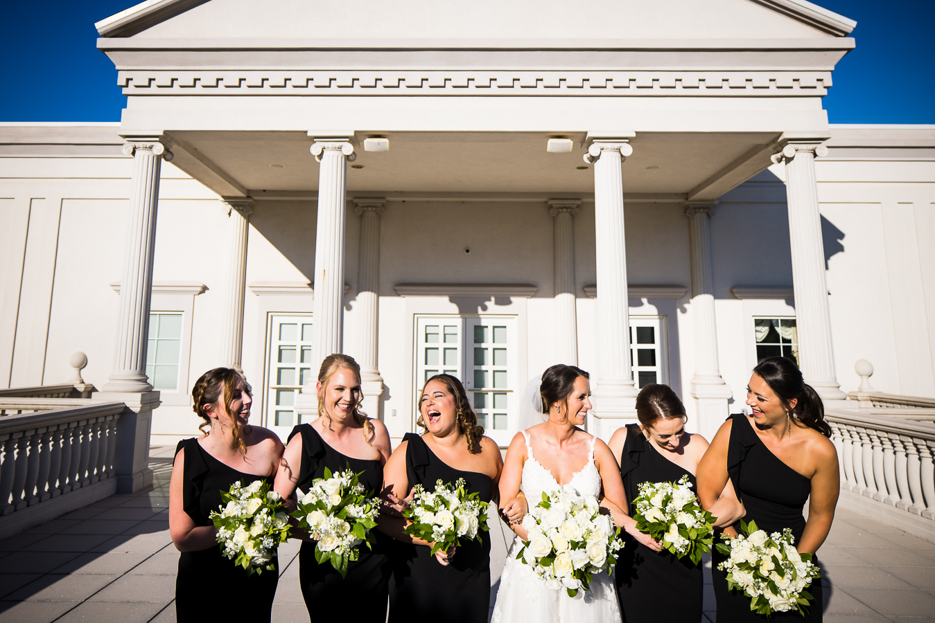 nj wedding photographer, lisa rhinehart, captures this fun, candid moment between the bride and her bridesmaids as they walk in front of the palace at somerset arm in arm laughing and smiling at each other in their black and white dresses