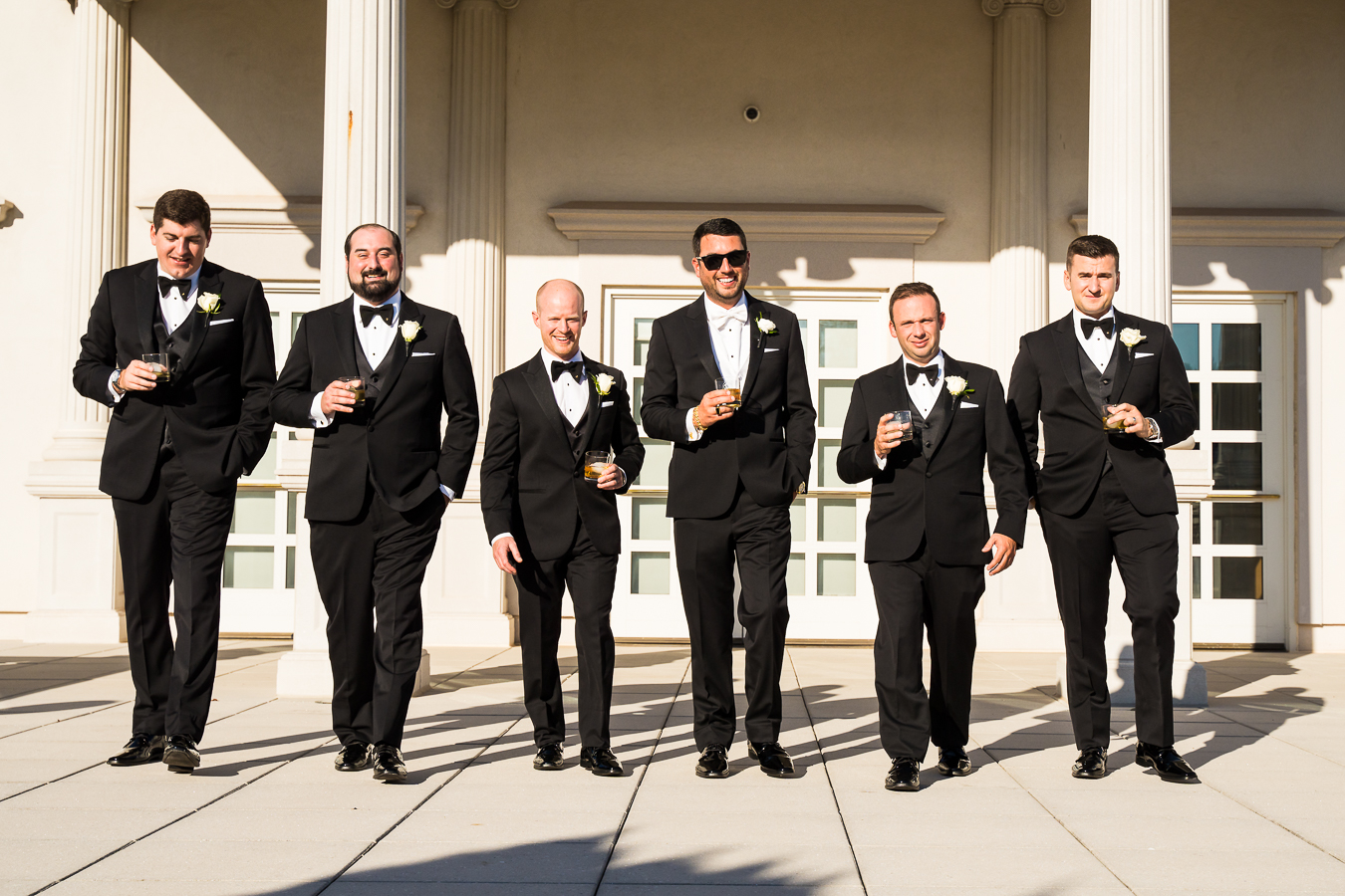 candid nj wedding photographer, lisa rhinehart, captures this fun image of the groom and his groomsmen as they walk in front of the palace at somerset park with drinks in their hand before their wedding ceremony 