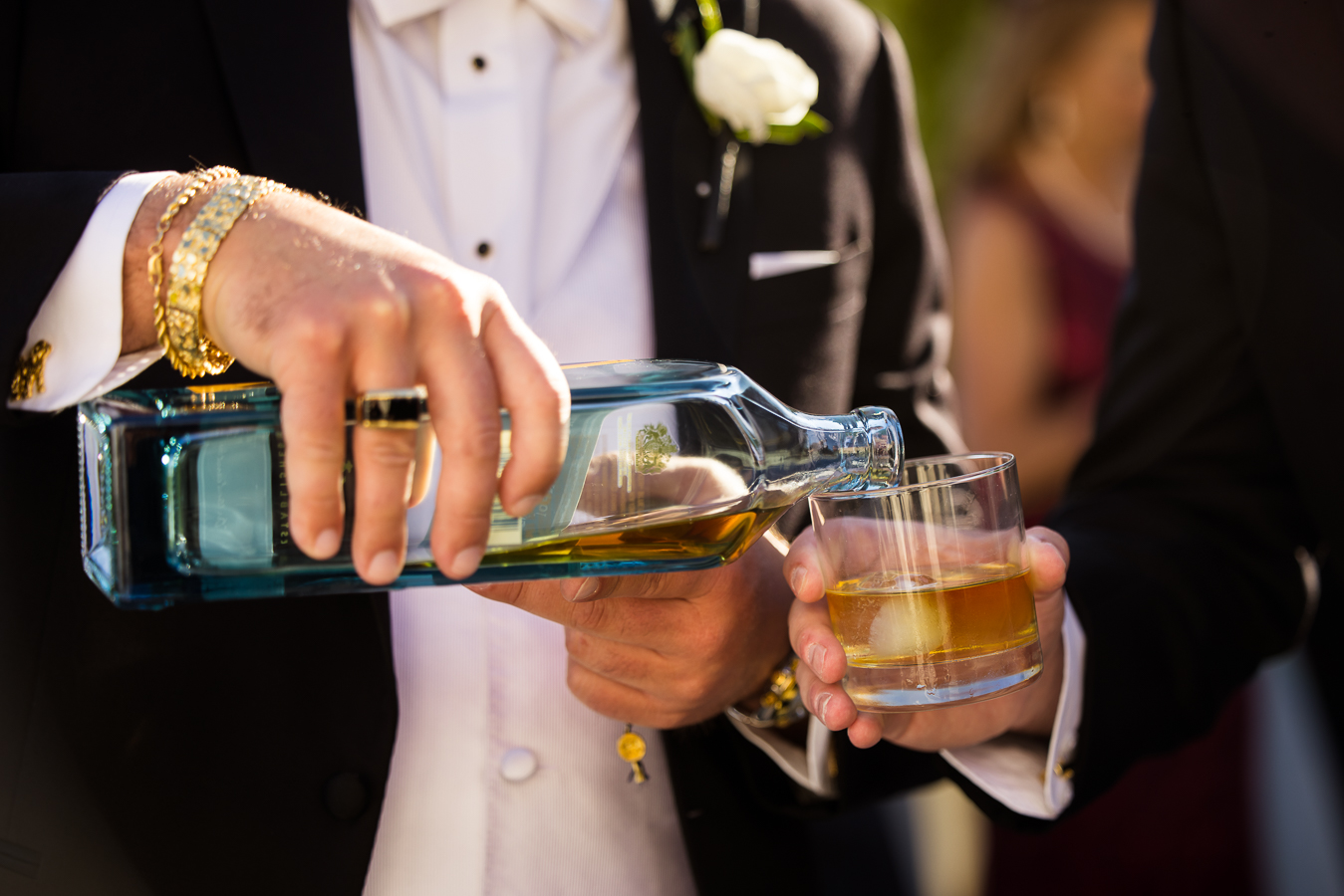 black and gold wedding inspiration: image of one groomsmen pouring alcohol into a glass for another groomsmen before the wedding ceremony at the palace at somerset park