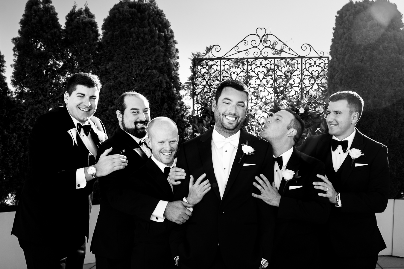 candid, creative, fun image of the groomsmen as they gather around the groom and make silly faces at him during these wedding party photos outside of the palace at somerset park in new jersey