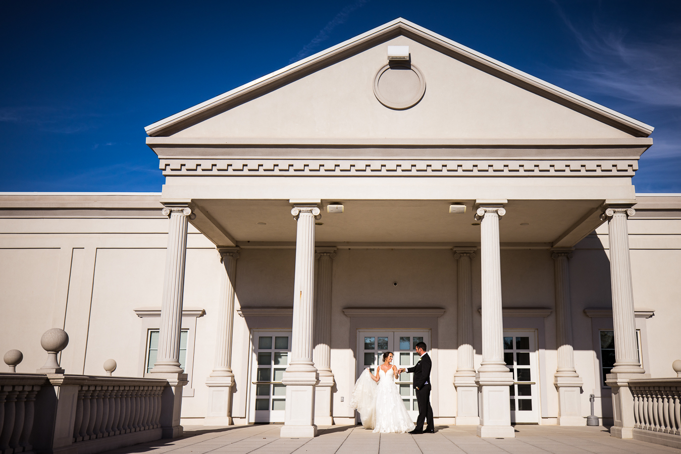 nj wedding photographer, lisa rhinehart, captures this vibrant image of the bride and groom as they stand holding hands underneath the overhang during their first look outside of the palace at somerset park during their black and gold wedding 