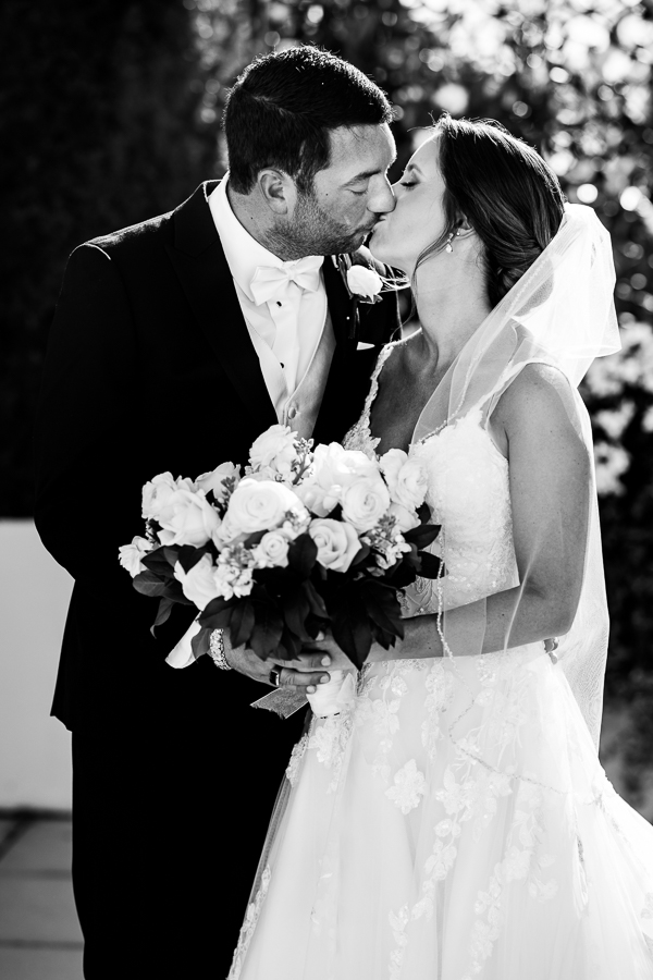 black and white image of this bride and groom as they share a kiss together during their outdoor first look at their black and gold wedding at the palace in somerset new jersey 