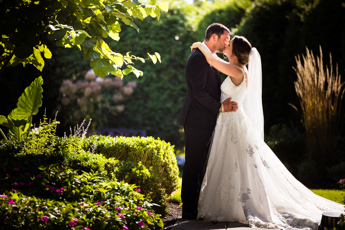 nj wedding photographer, lisa rhinehart, captures this vibrant, colorful image of the bride and groom as they share a kiss in the outdoor gardens at the palace at somerset park in new jersey 