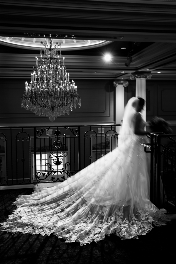 black and white image of the bride as she gets ready to walk down the stairs at her palace at somerset park wedding ceremony with a huge luxury chandelier hanging in the background behind her