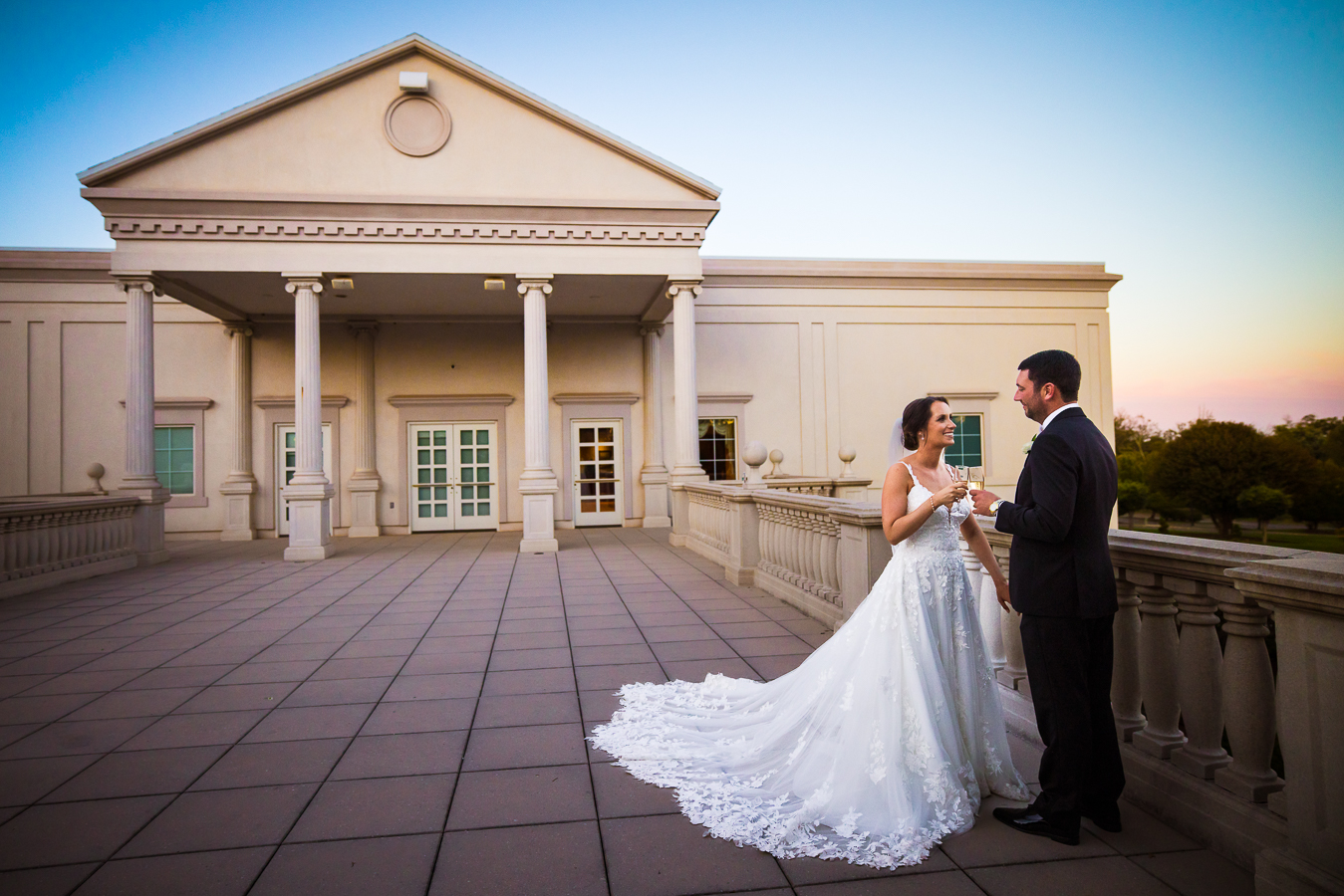 creative nj wedding photographer, lisa rhinehart, captures this unique, creative image of the bride and groom as they share a drink together outside of the palace at somerset park as the sun sets behind them and the sky has a mini rainbow before this black and gold wedding reception 